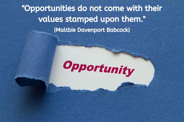 A navy blue piece of paper has a strip torn and folded back on itself so that a whole is exposed in the middle of the paper. Below that gap, is a white surface with the word Opportunity printed in red. The text reads: "Opportunities do not come with their values stamped upon them." (Maltbie Davenport Babcock)