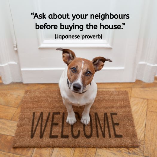 A small brown-and-white Jack Russell terrier sits on a doormat that says “WELCOME” in capital letters. Behind the dog is a white-painted door. The quote on the image reads: “Ask about your neighbours before buying the house.” (Japanese proverb)