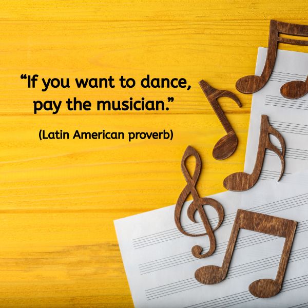 A vivid yellow wooden background with sheets of music and large wooden musical notes scattered across the frame. Overlaid black text reads: “If you want to dance, pay the musician.” (Latin American proverb)