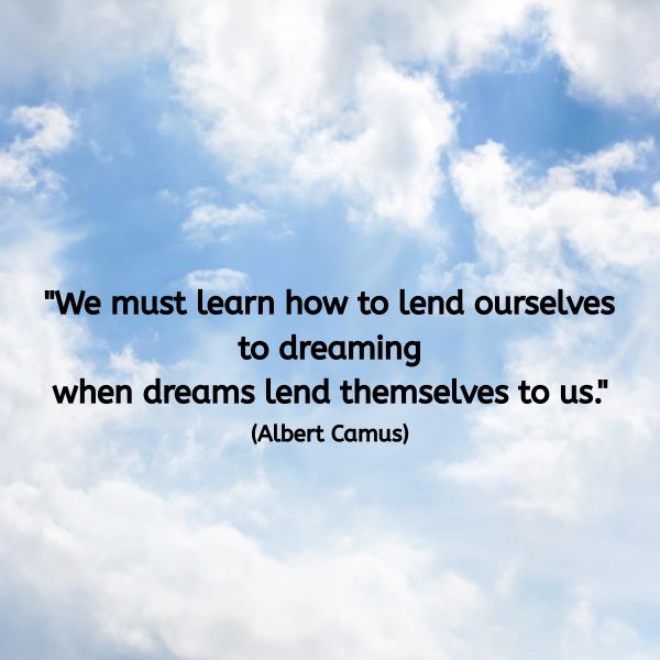 A soft blue sky filled with gentle, white clouds. Some clouds are bright and fluffy, while others form subtle layers across the sky, creating a sense of openness and quiet movement. In the centre of the image, overlaid in black text, is the quote: “We must learn how to lend ourselves to dreaming when dreams lend themselves to us.” (Albert Camus)