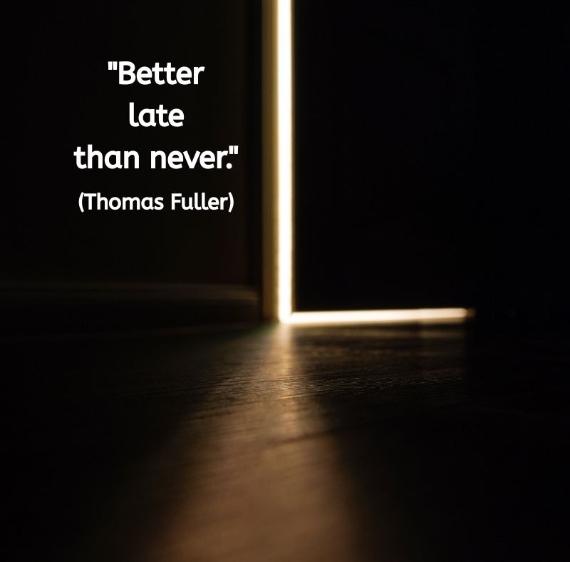A dark room with a single door slightly ajar. Warm light shines through the gap, illuminating part of the wooden floor. The quote text reads: "Better late than never." (Thomas Fuller).